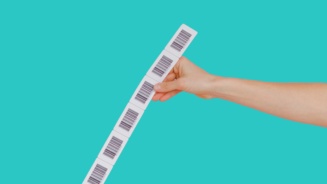 Hand hält einen langen Streifen mit mehreren Barcode-Etiketten vor türkisfarbenem Hintergrund