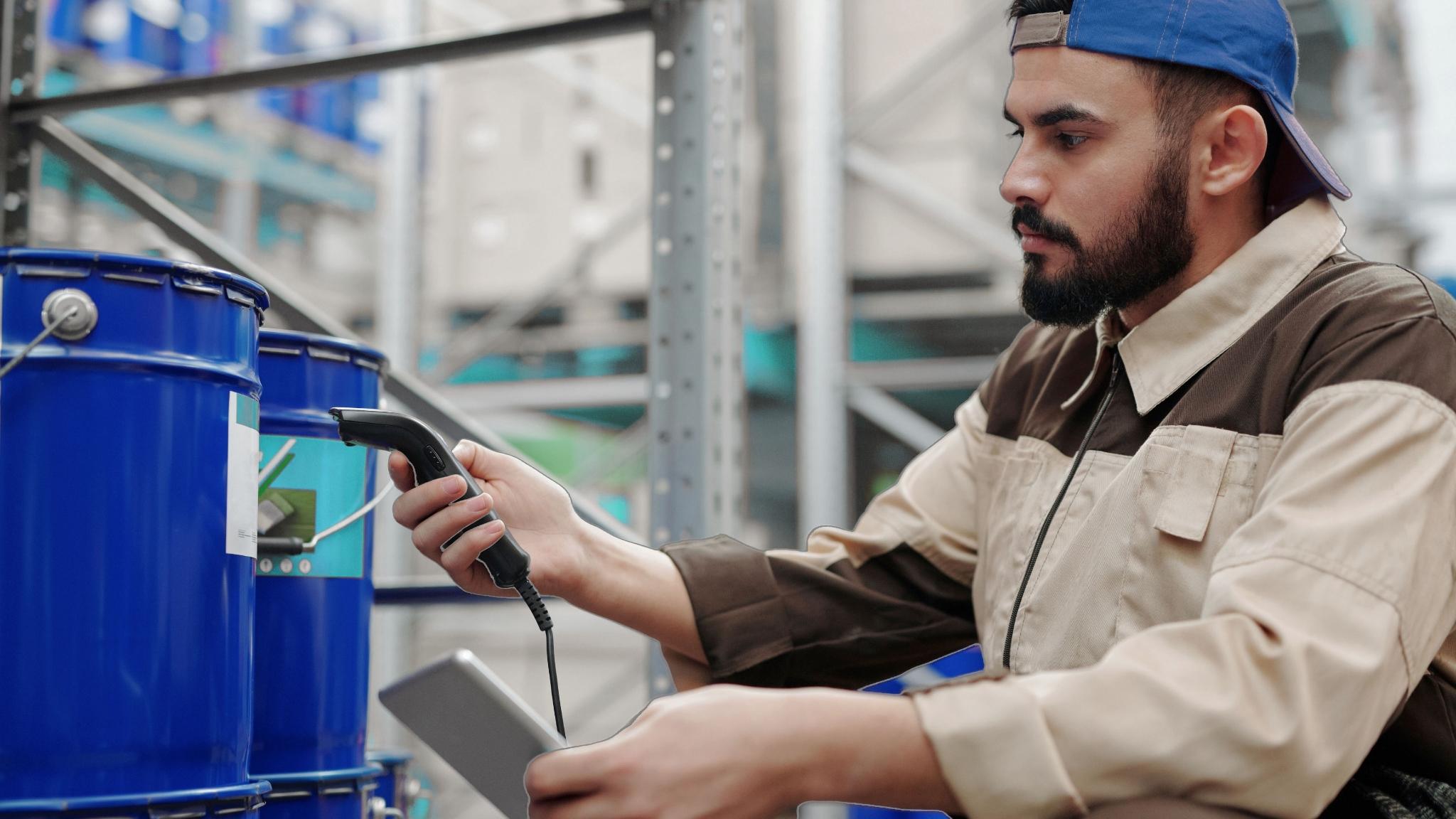 Lagerarbeiter scannt Barcode auf blauem Fass mit kabelgebundenem Handscanner – industrielle Kennzeichnung und Bestandserfassung