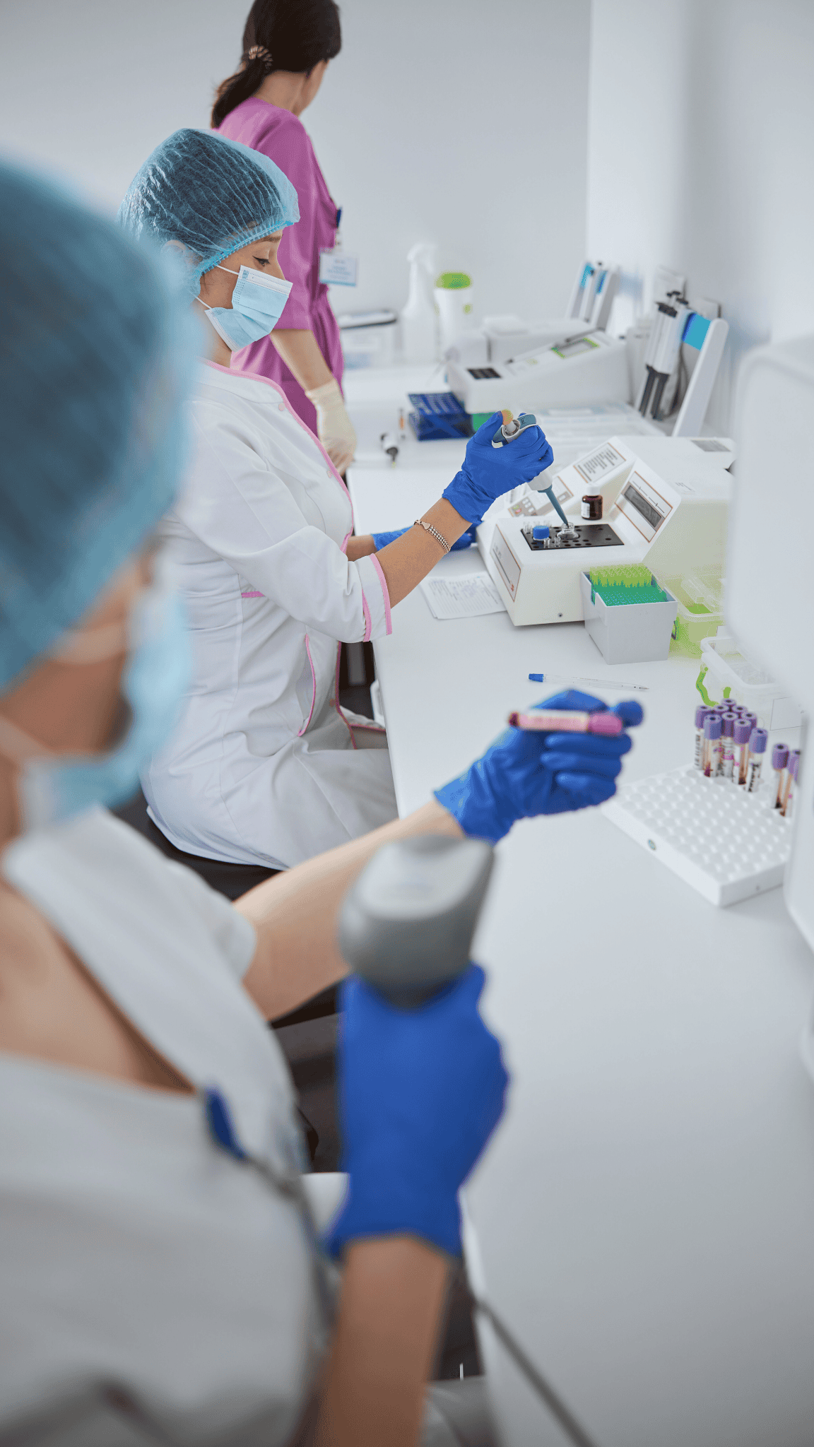 Labormitarbeiterinnen mit Schutzkleidung und Handschuhen bei der Analyse von Blutproben im medizinischen Labor